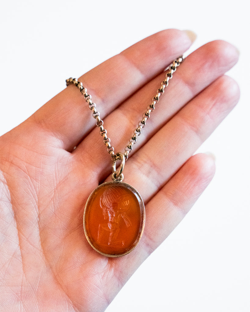 Victorian era carnelian intaglio pendant, in 15k gold.The carving depicts Atlas holding the sky, representing endurance, strength, or commitment. English in Origin. Circa 1830. A hand holding the pendant for scale. 