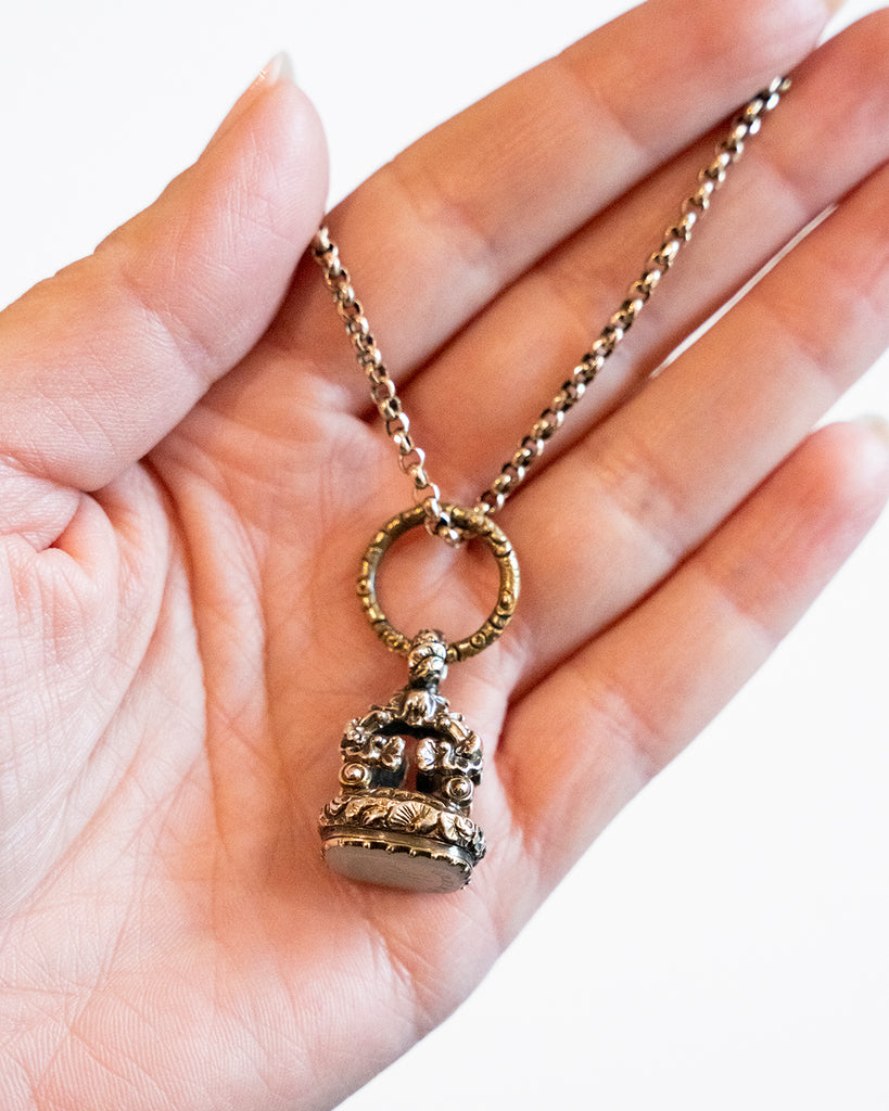 Victorian era watch fob in 9k gold. Carved white agate seal with a rebus puzzle depicting the word “friend” and a ship. English in origin. Circa 1880. Being held in a hand for scale. 