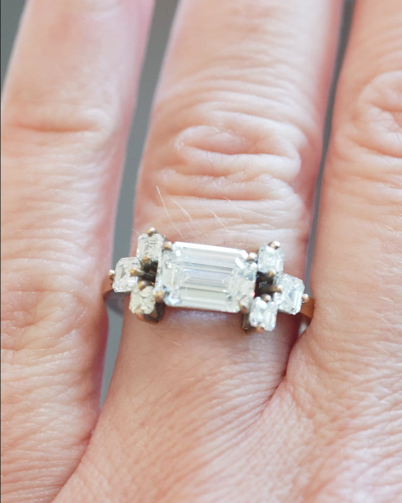 This seven stone ring was inspired by a 17th century diamond ring that we once had. The arrangement is characteristic of rings that date from 1650-1700. This ring features a GIA certified 2.05 carat emerald cut diamond, E color and VVS1 clarity. There are six Asscher cut diamonds, approximately .79 carats in total diamond weight, F color, and VS1/VS2 clarity. It was handcrafted in our 18k old gold. A video of the ring bing modeled. 